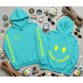 Turquoise hoodie with 'Pali Adventures' and 'Happy Camper' text, surrounded by camping-themed items on a light gray background.